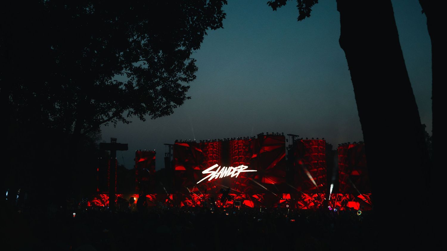 Red neon text glows against a dark background with silhouetted trees creating a moody nighttime atmosphere.