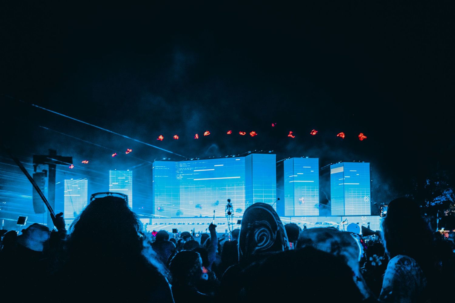 Concert venue illuminated in blue lighting with silhouettes of crowd and stage equipment visible.