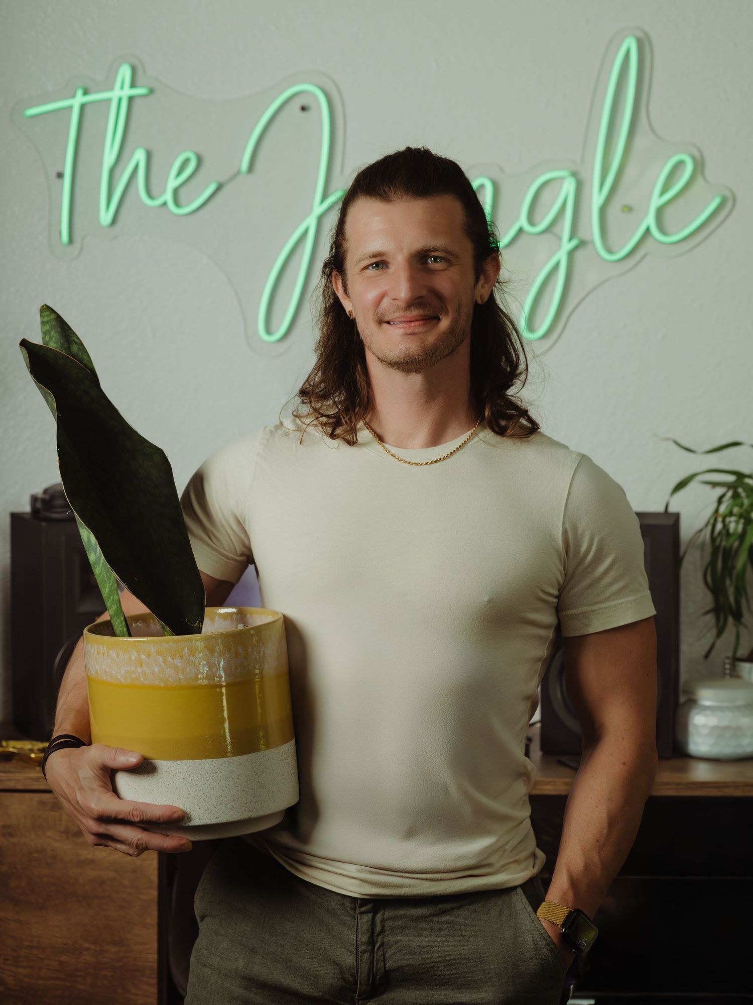 A person in a beige shirt stands in a cafe interior with green neon signage on the wall.