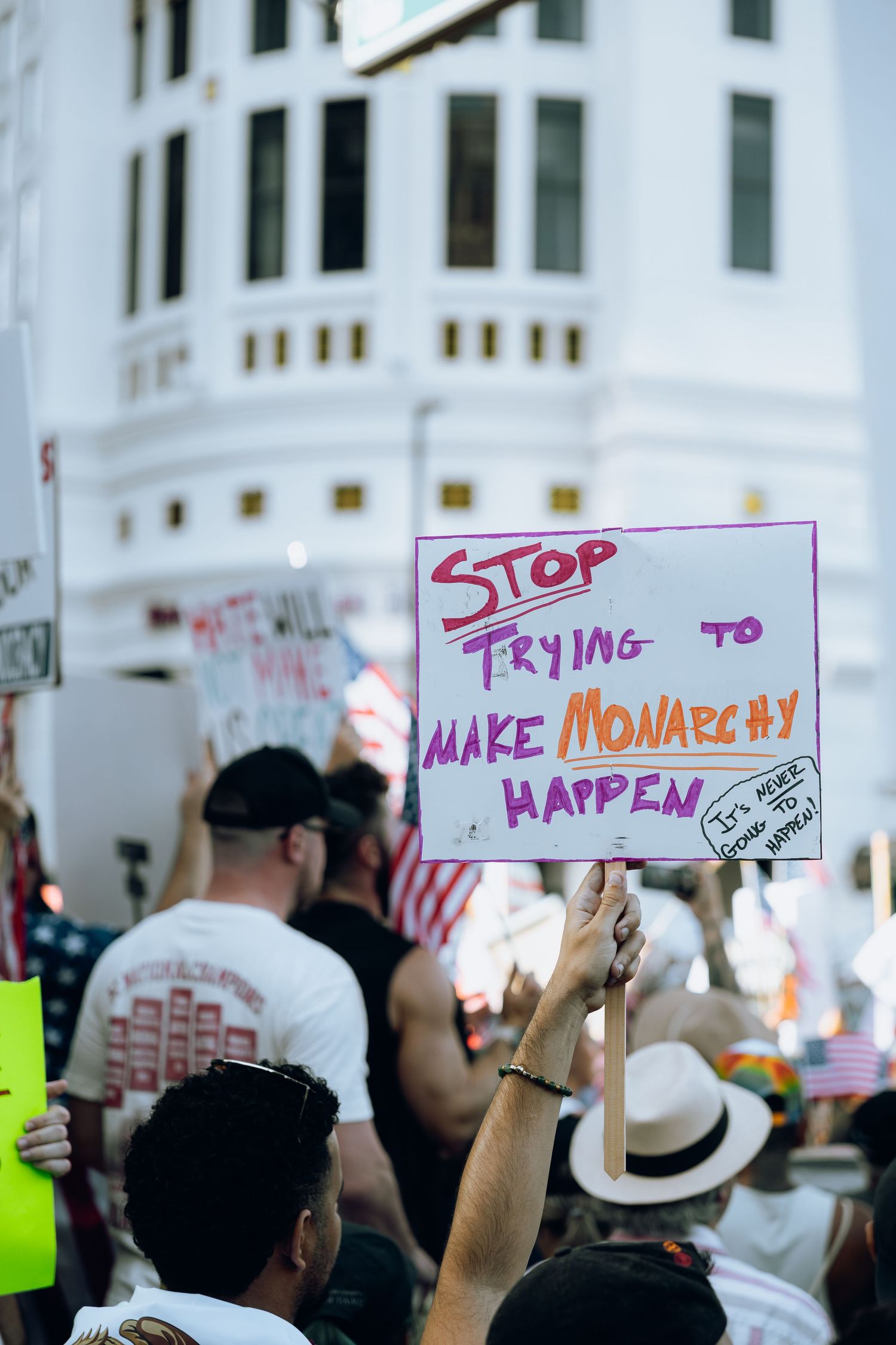 A protest sign reading 'Stop trying to make monarchy happen' held up among a crowd of demonstrators at a rally.