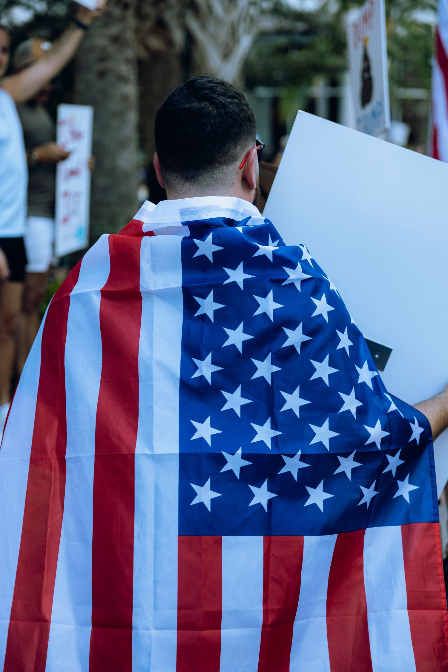 Protester draped in American flag holding blank sign at political demonstration.