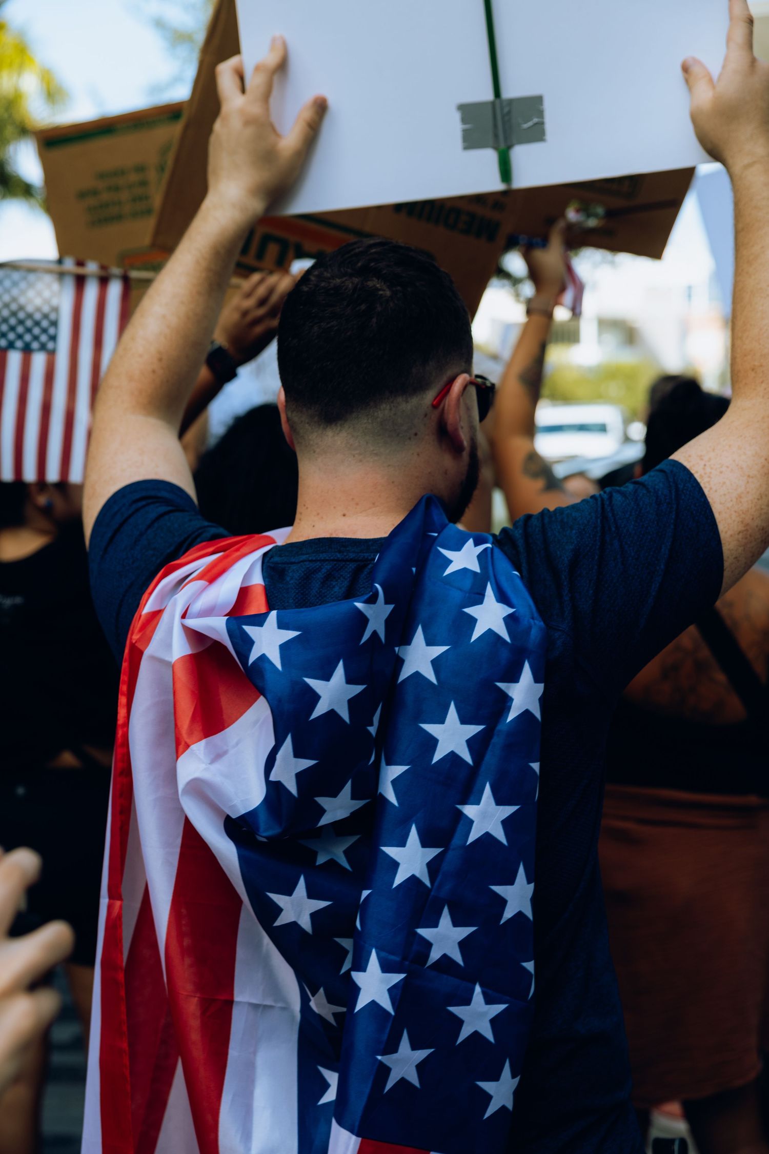 Protester wearing American flag cape raises hands during demonstration.