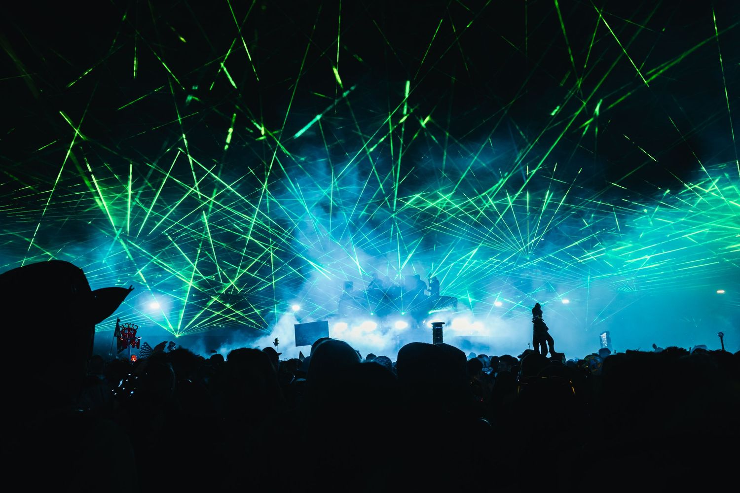 Green laser beams illuminate a dark night sky above a silhouetted cityscape creating a dramatic light show effect.