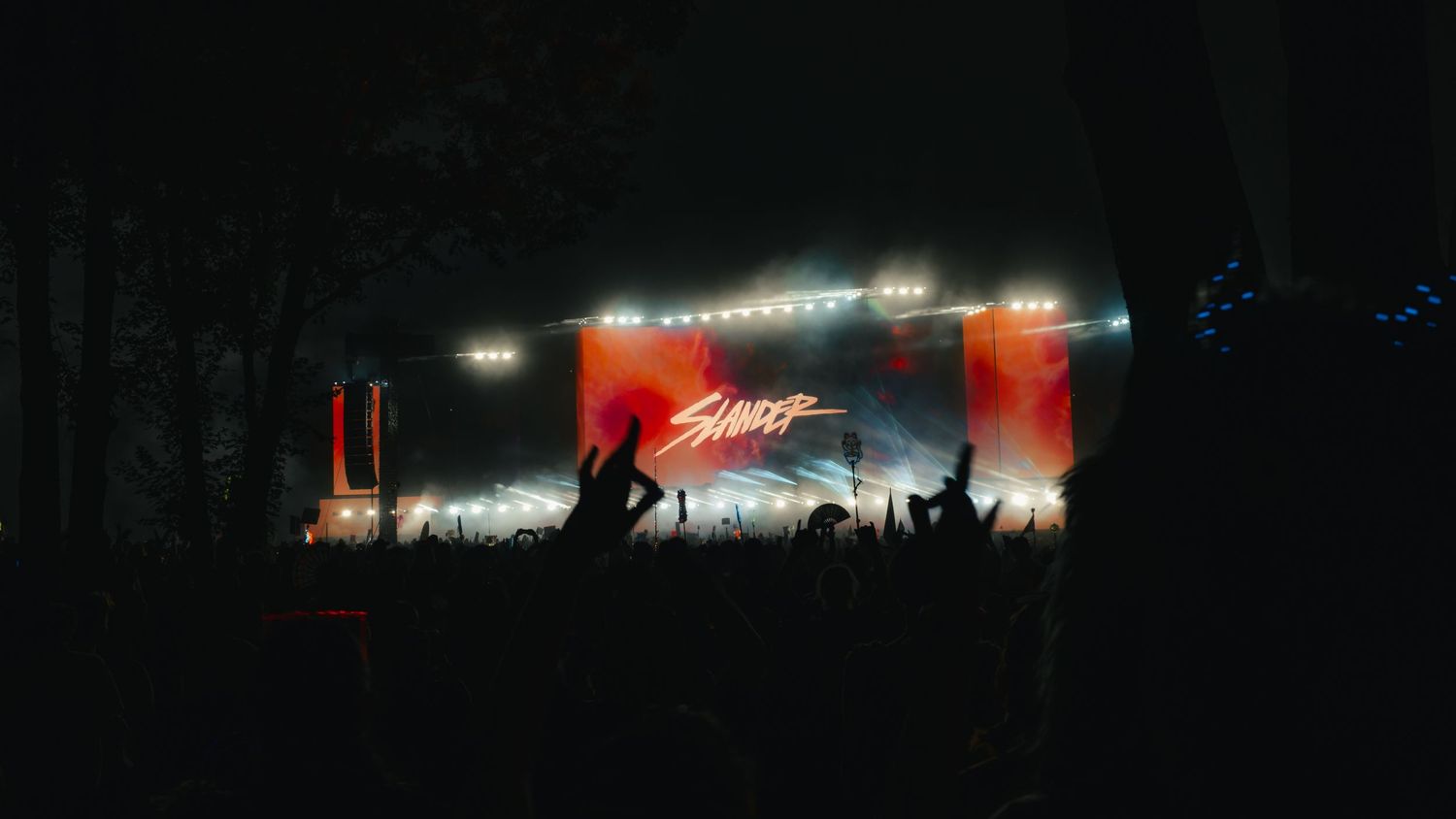 Concert crowd silhouettes against a red-lit stage with bright lights and signage during a nighttime performance.