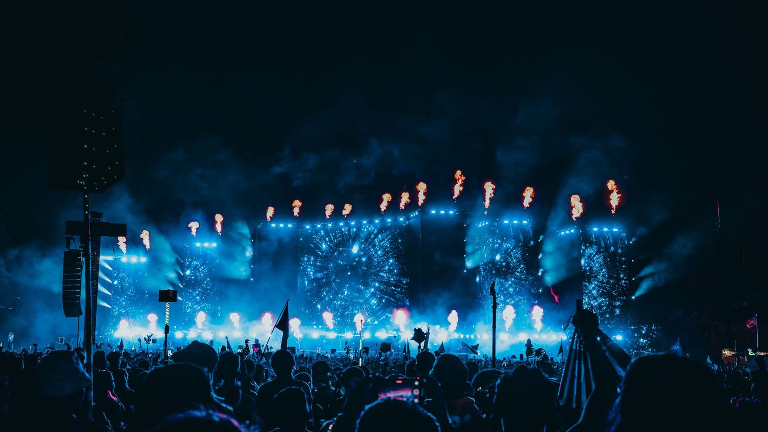 Concert stage illuminated with dramatic blue lighting and fog effects as silhouetted crowd watches performance.