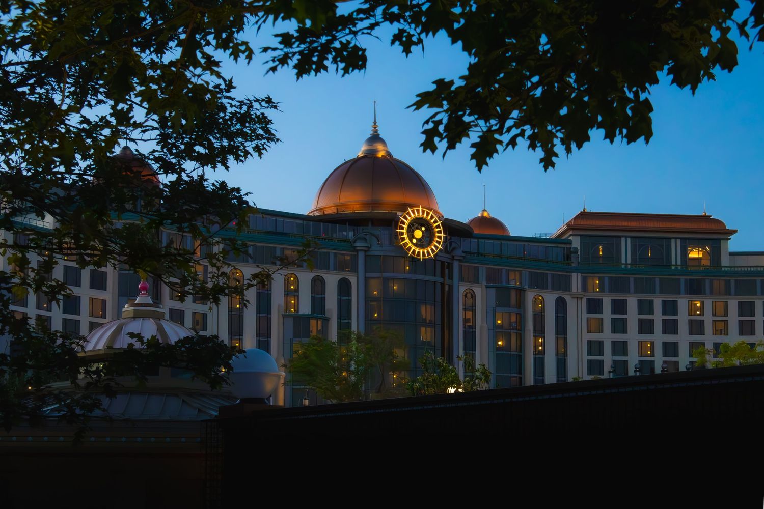 An illuminated domed building with classical architecture glows at dusk with trees framing the view.