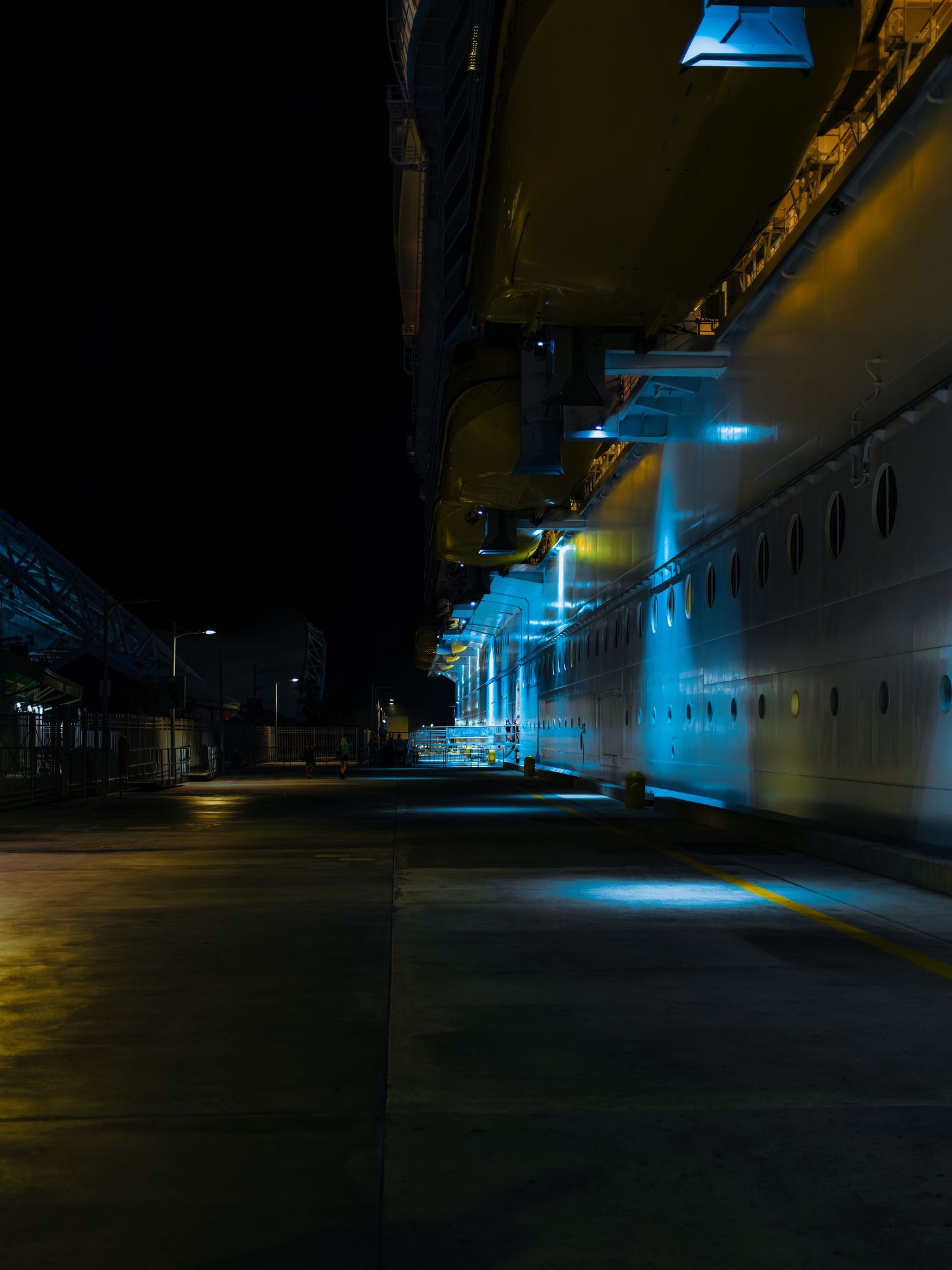 Dark corridor illuminated by eerie blue lights casting dramatic shadows along empty industrial hallways.