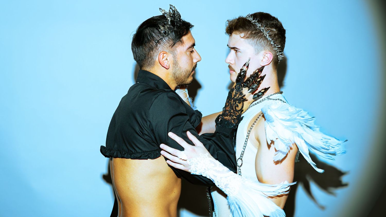 Two dancers perform a dramatic contemporary dance sequence in silhouette against a light blue background.