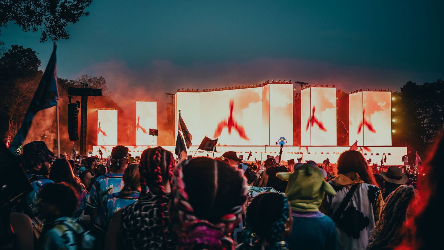A panoramic view of a dimly lit concert venue with red stage lighting and silhouetted crowd in attendance.