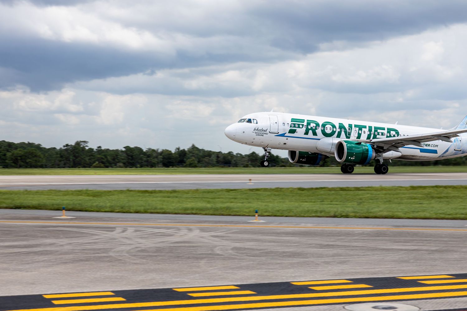 Frontier Airlines aircraft taxiing on runway with green tail livery under cloudy skies.