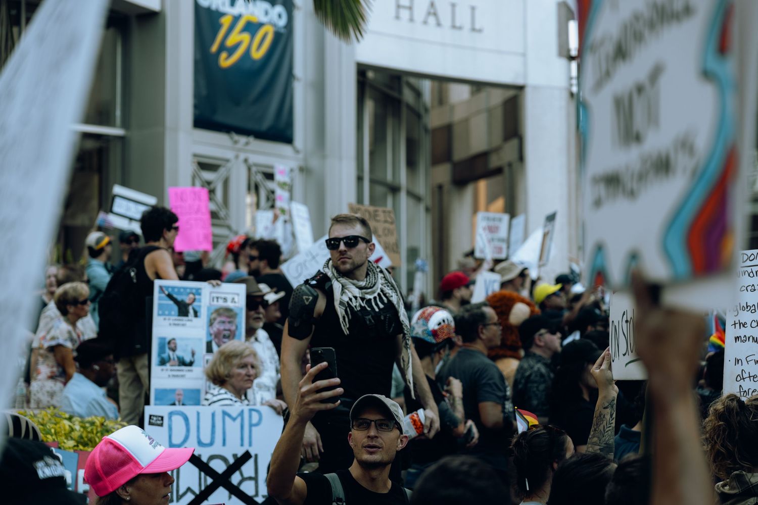 Demonstrators gather in a city street holding protest signs and wearing face coverings during a rally.