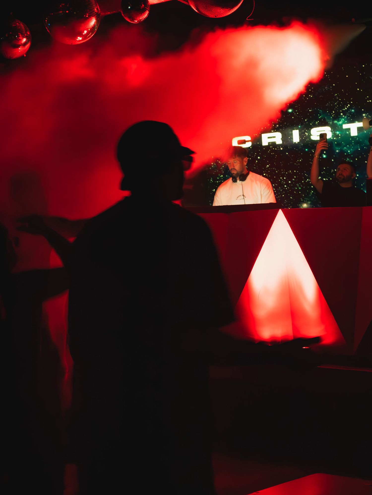 A silhouette stands in a nightclub with red lighting and illuminated geometric shapes under a neon 'GRID' sign.