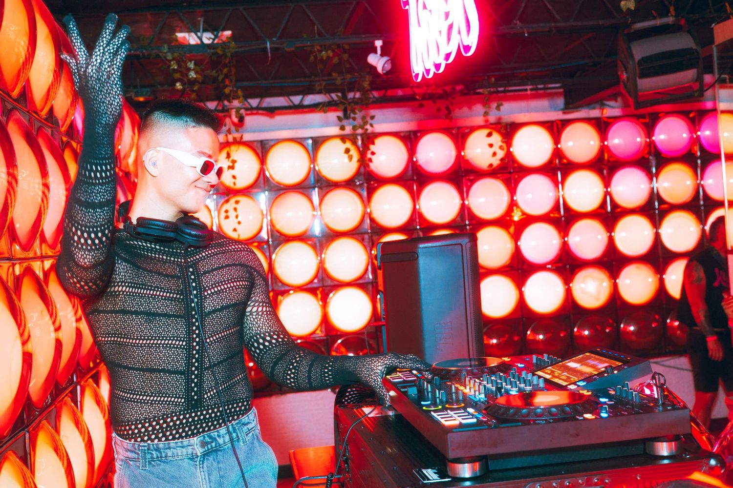Female DJ performing on stage with bright stage lights in a nightclub.