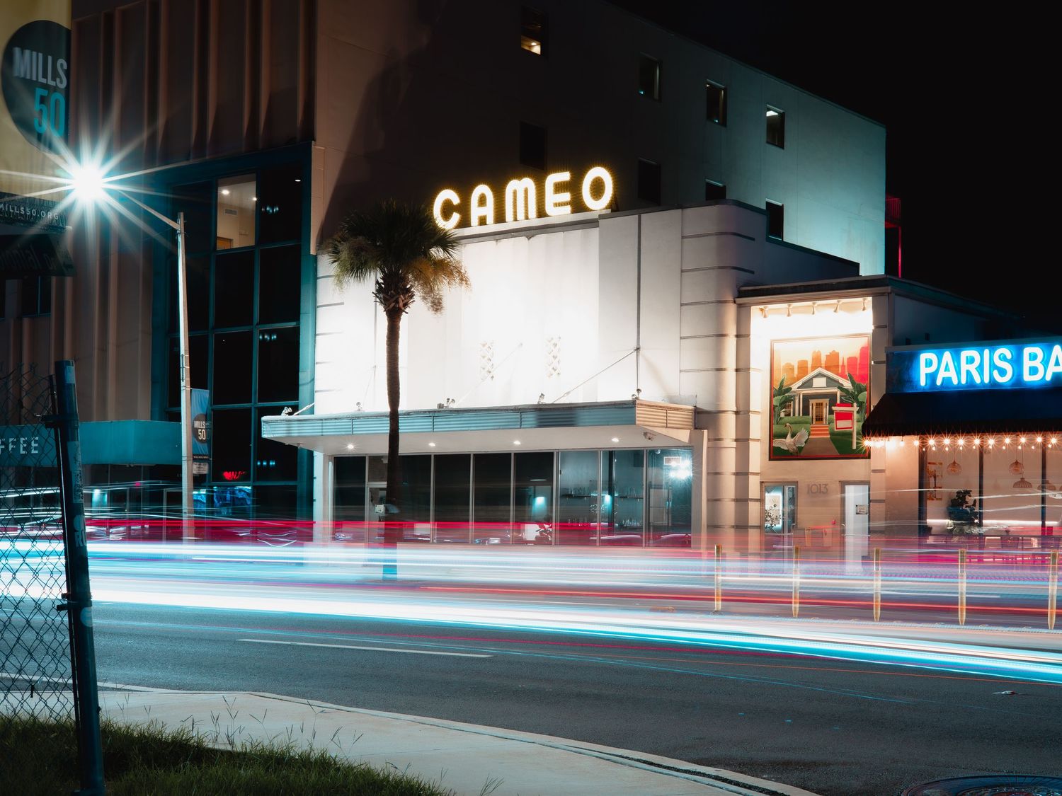 Long exposure night cityscape with streaking car lights and neon signs illuminating dark urban streets.