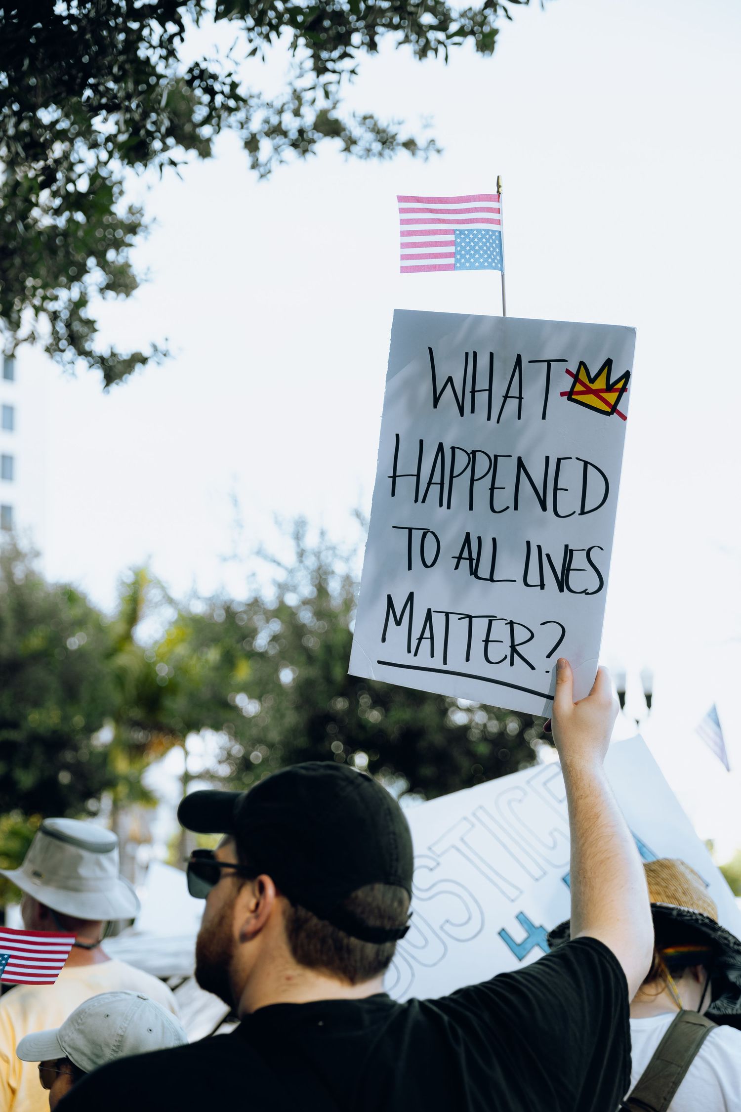 Protesters raise signs with messages about justice and equality against a bright sky background.