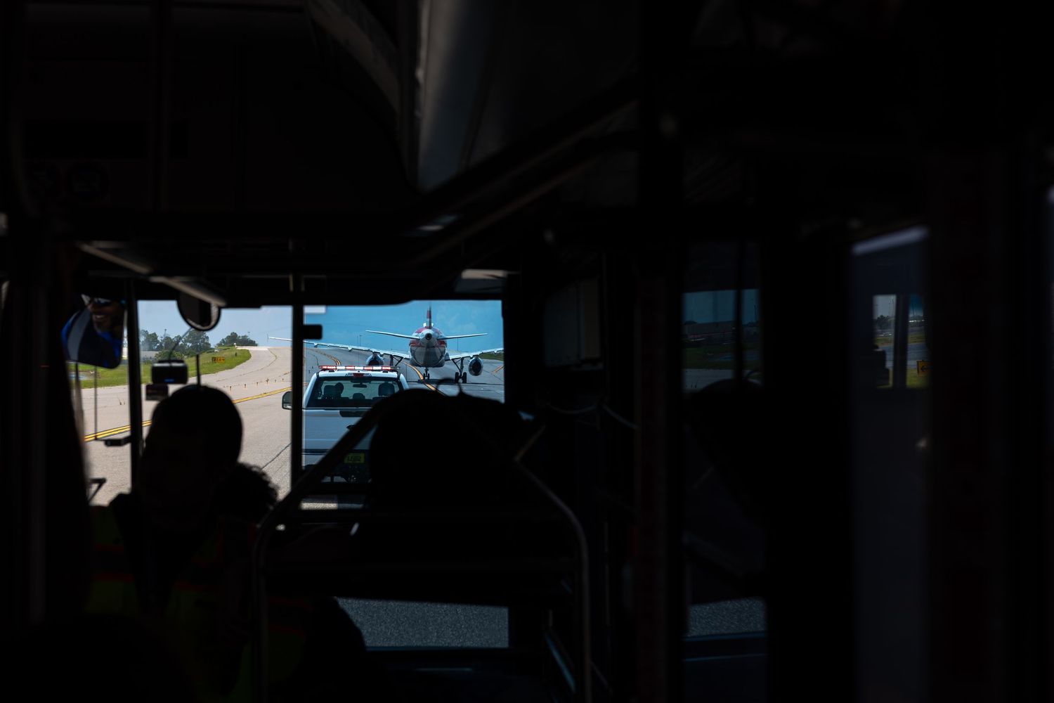 View from inside a bus at an airport tarmac with a passenger airplane visible through the windshield.
