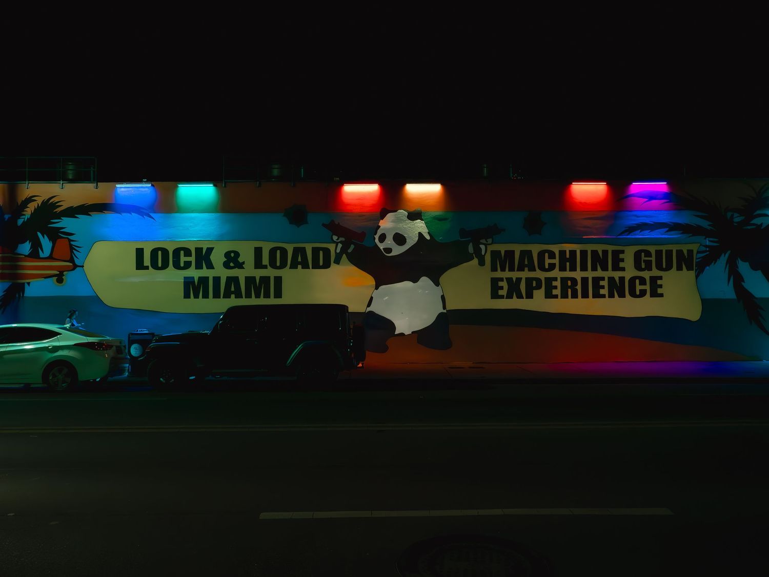 Neon-lit sign for Lock & Load Miami machine gun experience featuring a panda mascot glowing at night.