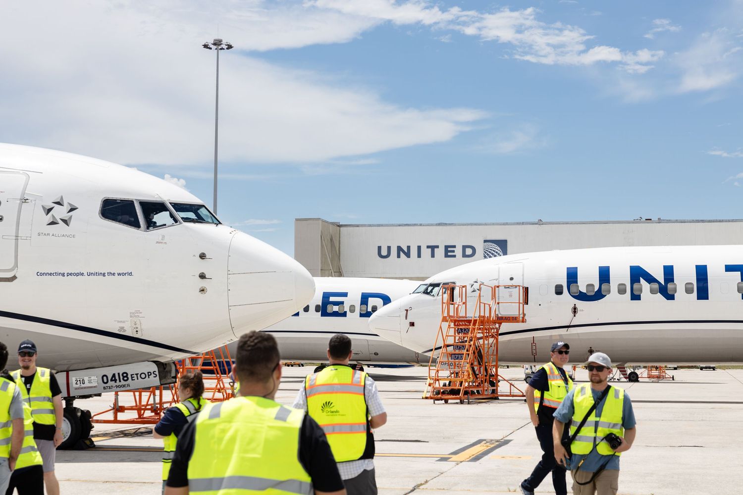 United Airlines ground crew workers in yellow vests on airport tarmac near parked commercial aircraft.