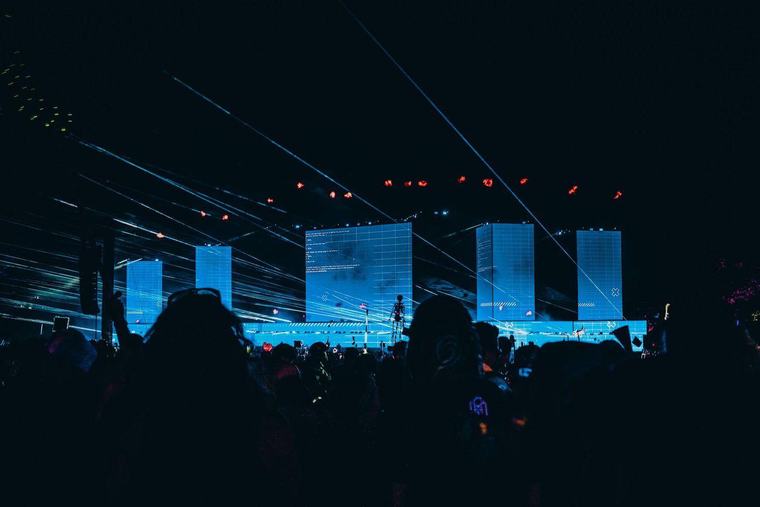 Concert venue illuminated with blue stage lights and silhouetted crowd during a live performance.