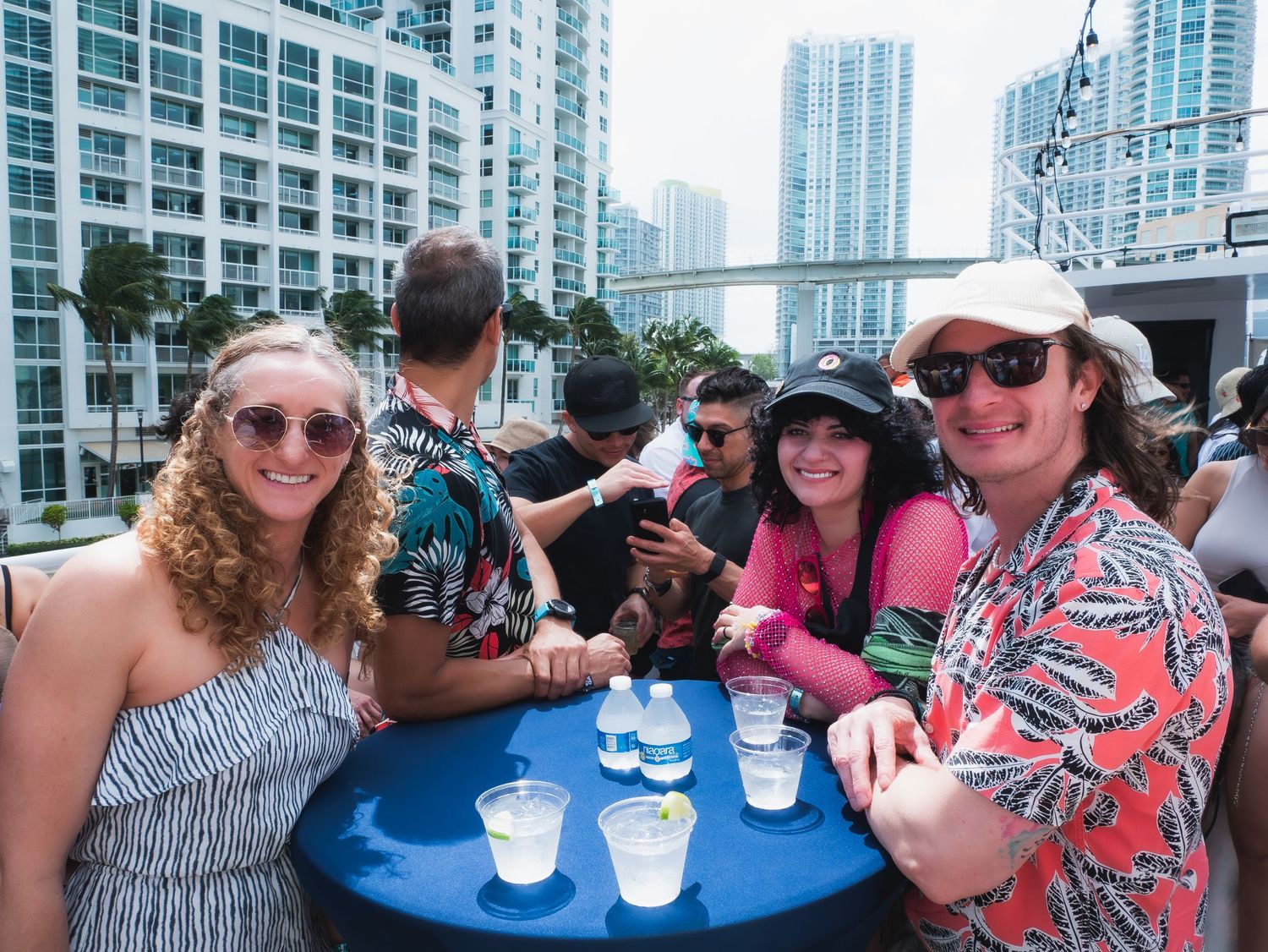 A group of people enjoying drinks at a rooftop bar with Miami high-rise buildings in the background.