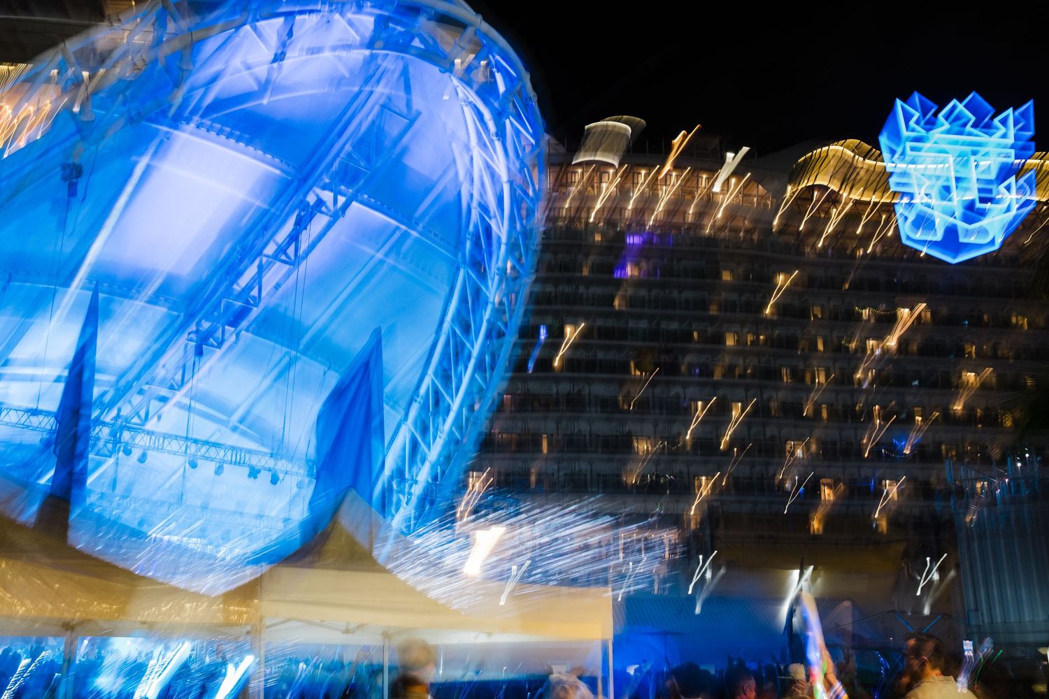 Blurred motion shot of blue illuminated cruise ship exterior at night with glowing deck lights.