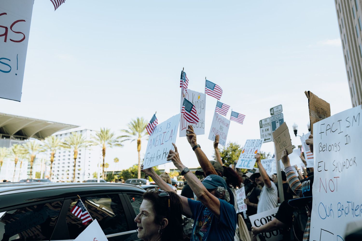 Crowd of protesters waving American flags and signs in front of urban building.