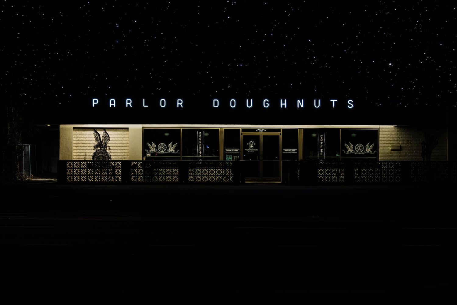 Parlor Doughnuts storefront illuminated at night with bright signage against a dark sky.