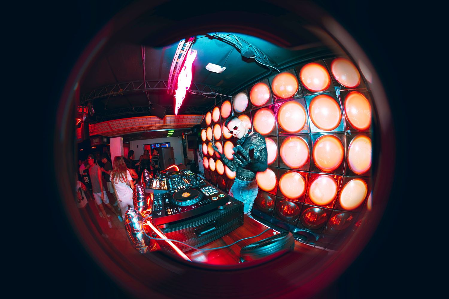 DJ performing at a nightclub with glowing orange lights and fisheye lens effect creating a vibrant atmosphere.
