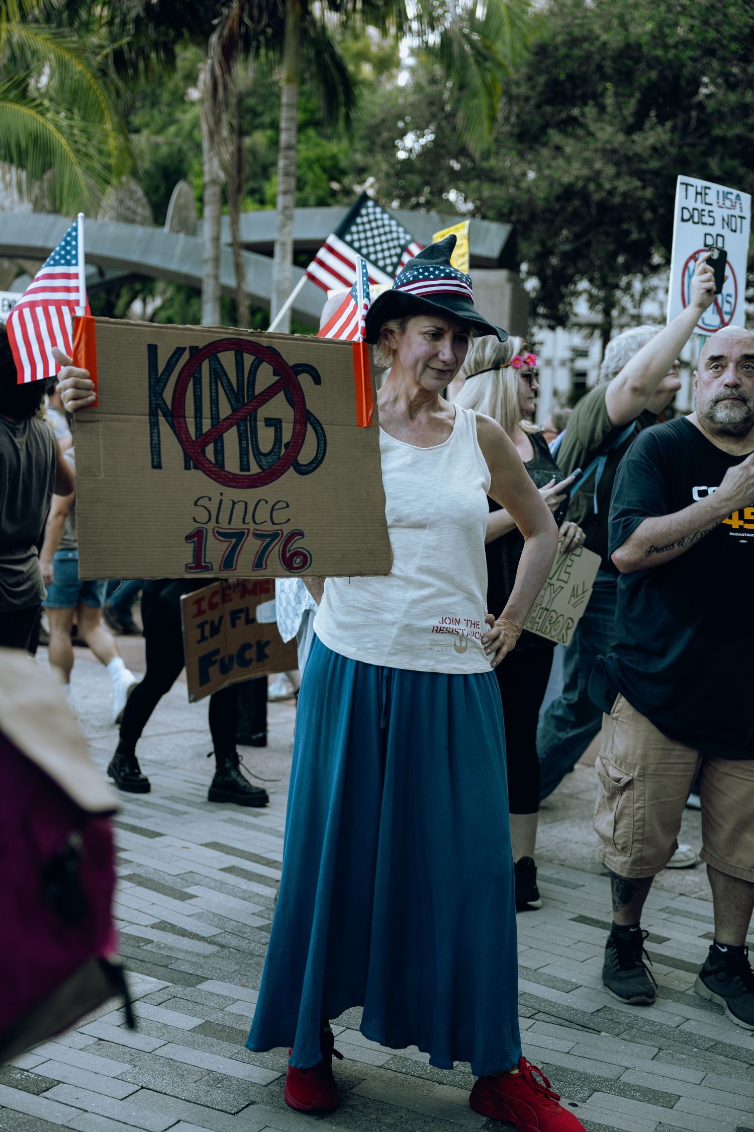Demonstrator holding protest sign at rally with American flags visible in background.