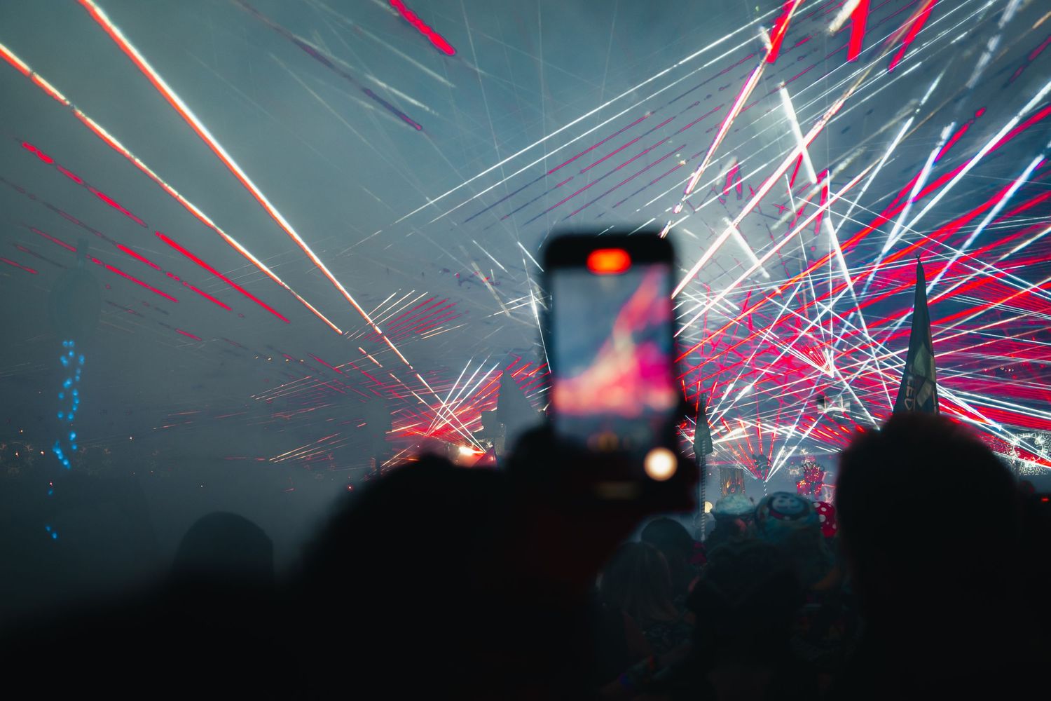A dark silhouette of a crowd watching a fireworks display with bright red and white streaks across the night sky.