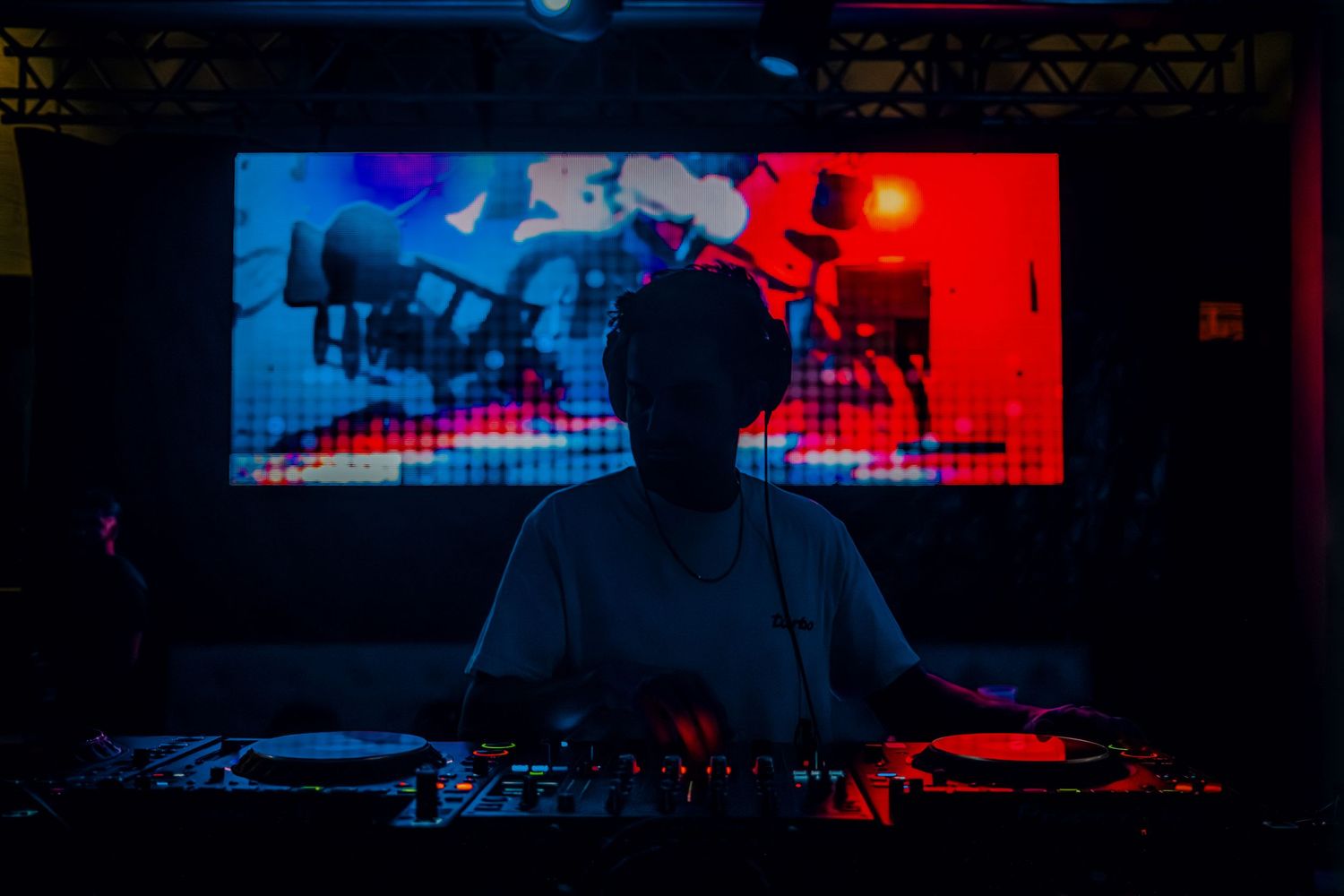 DJ performing at a nightclub with colorful red and blue lighting while mixing music on professional equipment.