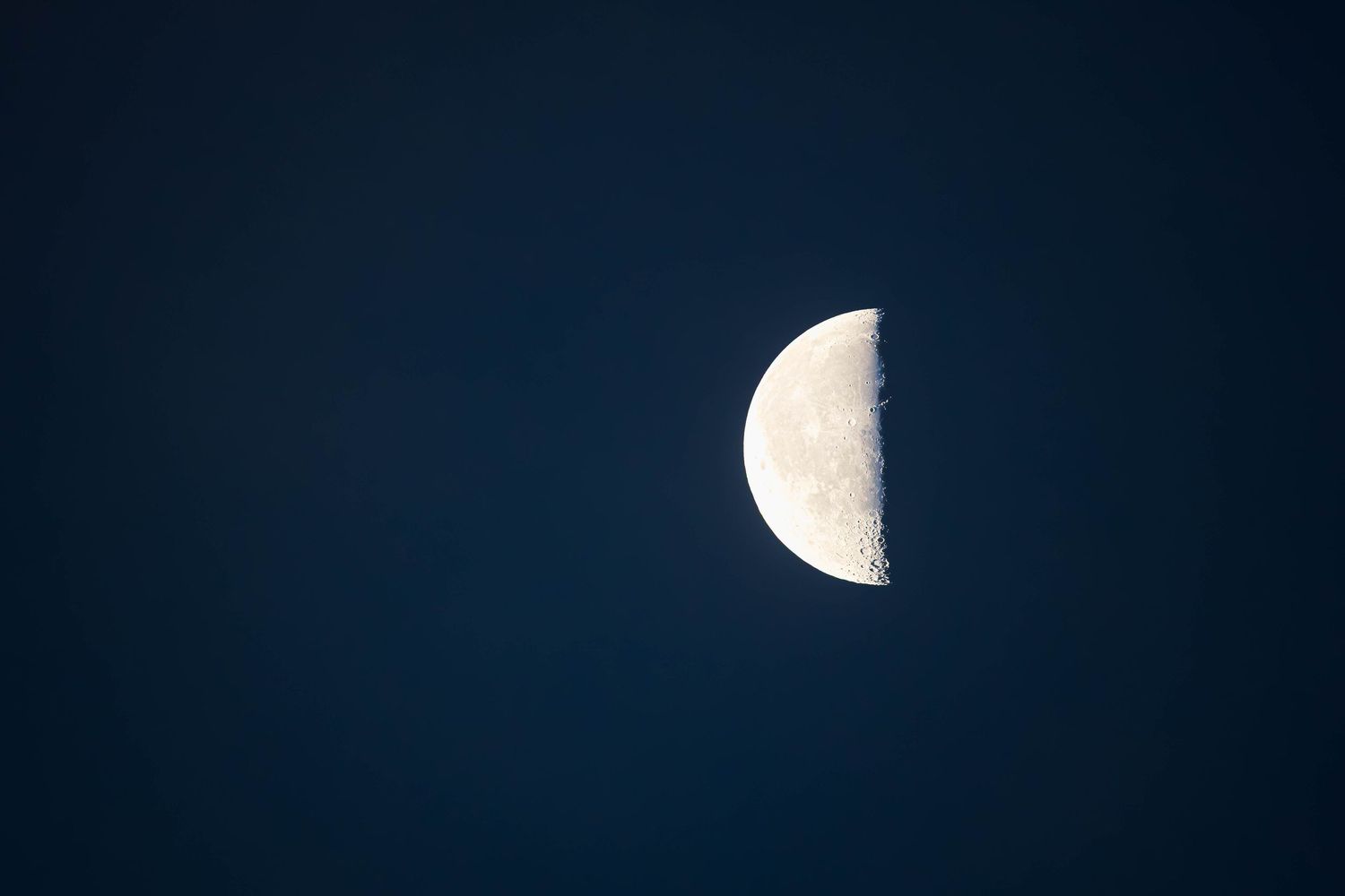 Half moon phase against dark blue night sky, detailed lunar surface visible.
