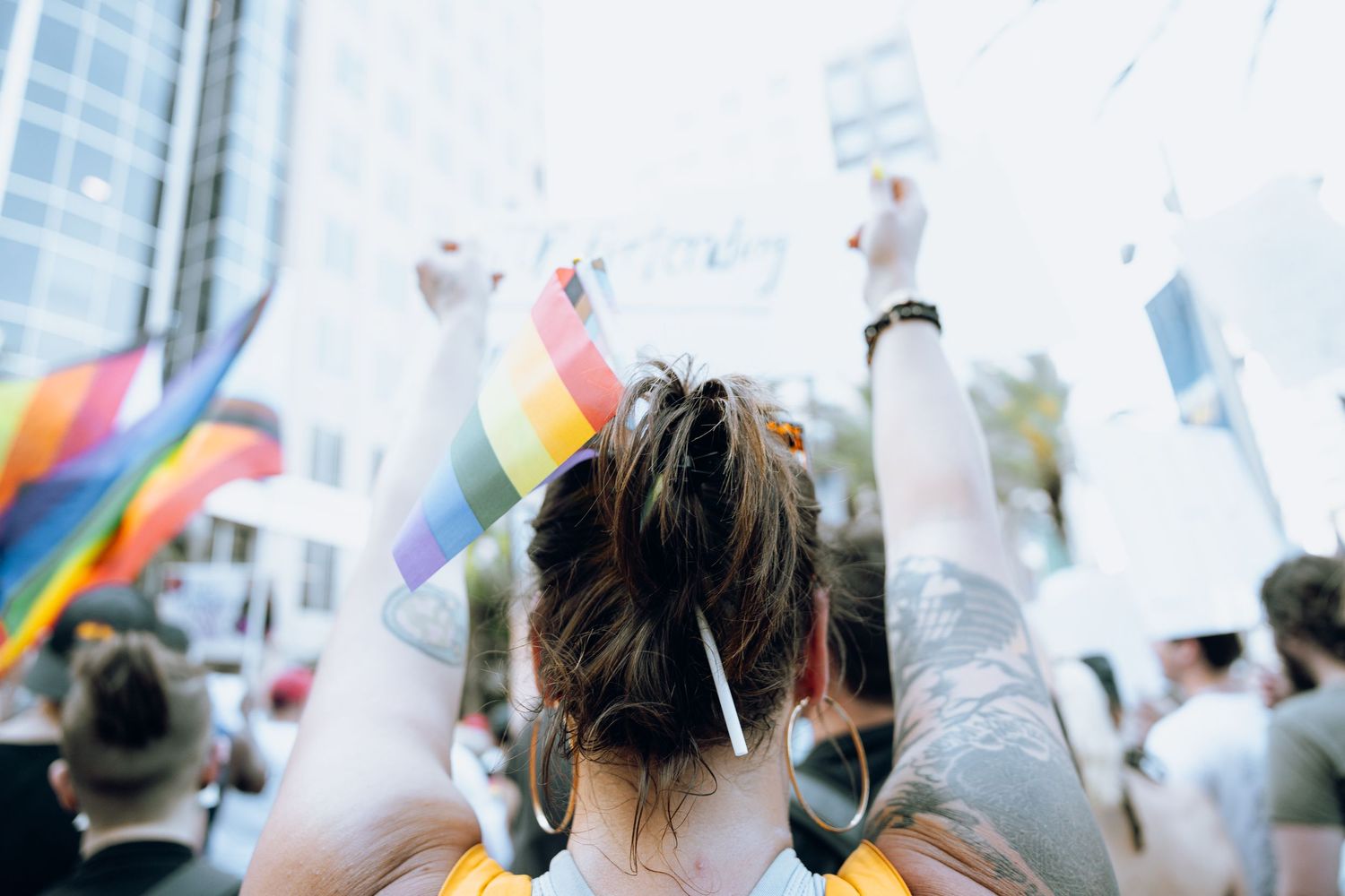 Rainbow and white flags being waved in a crowd at an outdoor demonstration or event.