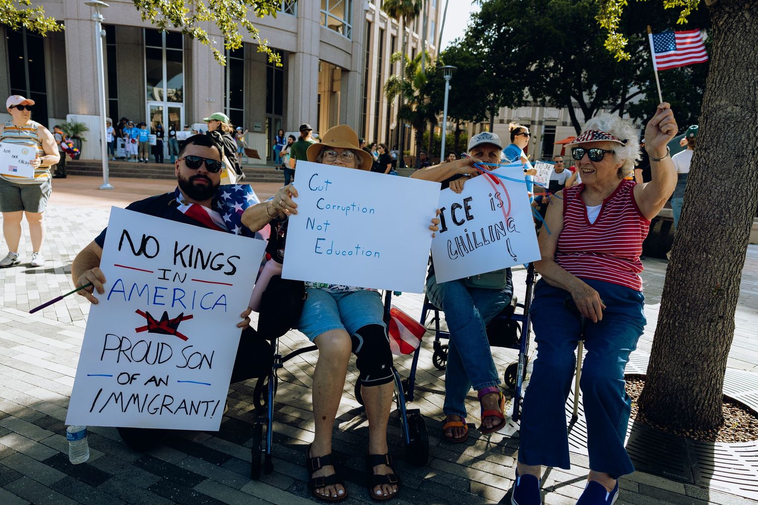 Protesters gather on a sidewalk holding signs during a demonstration outside a building.