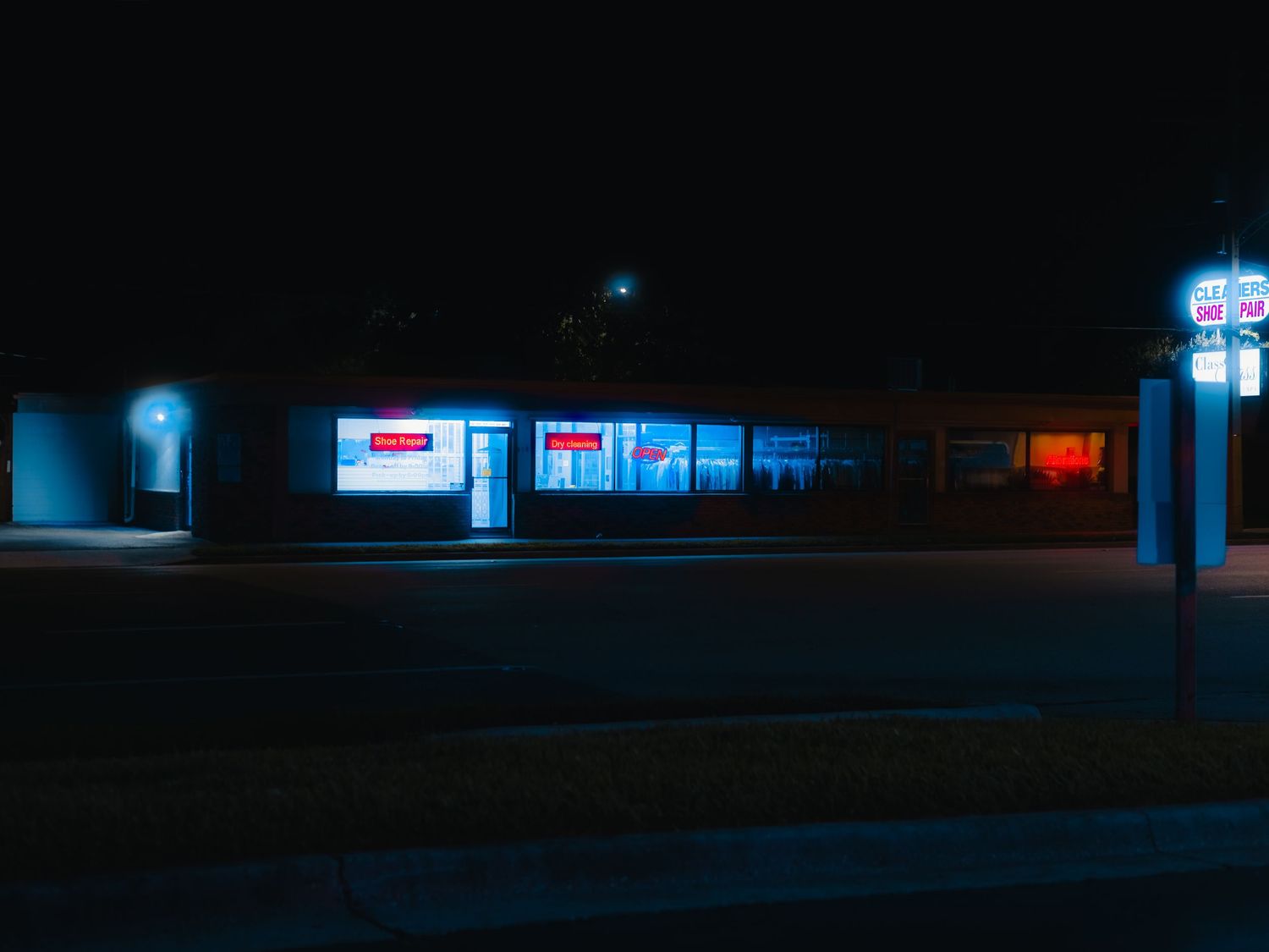 Illuminated storefront signs and business lights glowing in a dark strip mall at night.