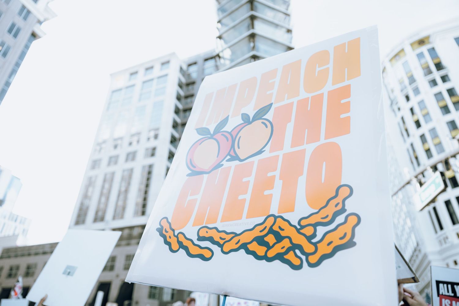 White protest sign with orange peach design against urban skyline.