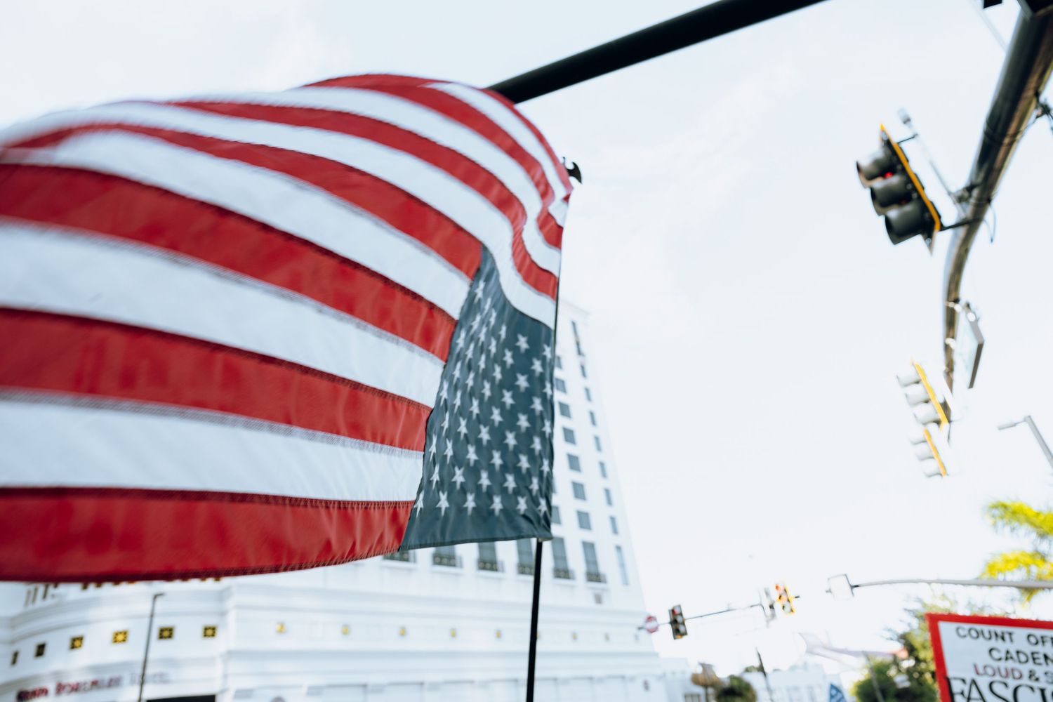 Looking up at a waving American flag against a blue sky with a traffic light in the background.