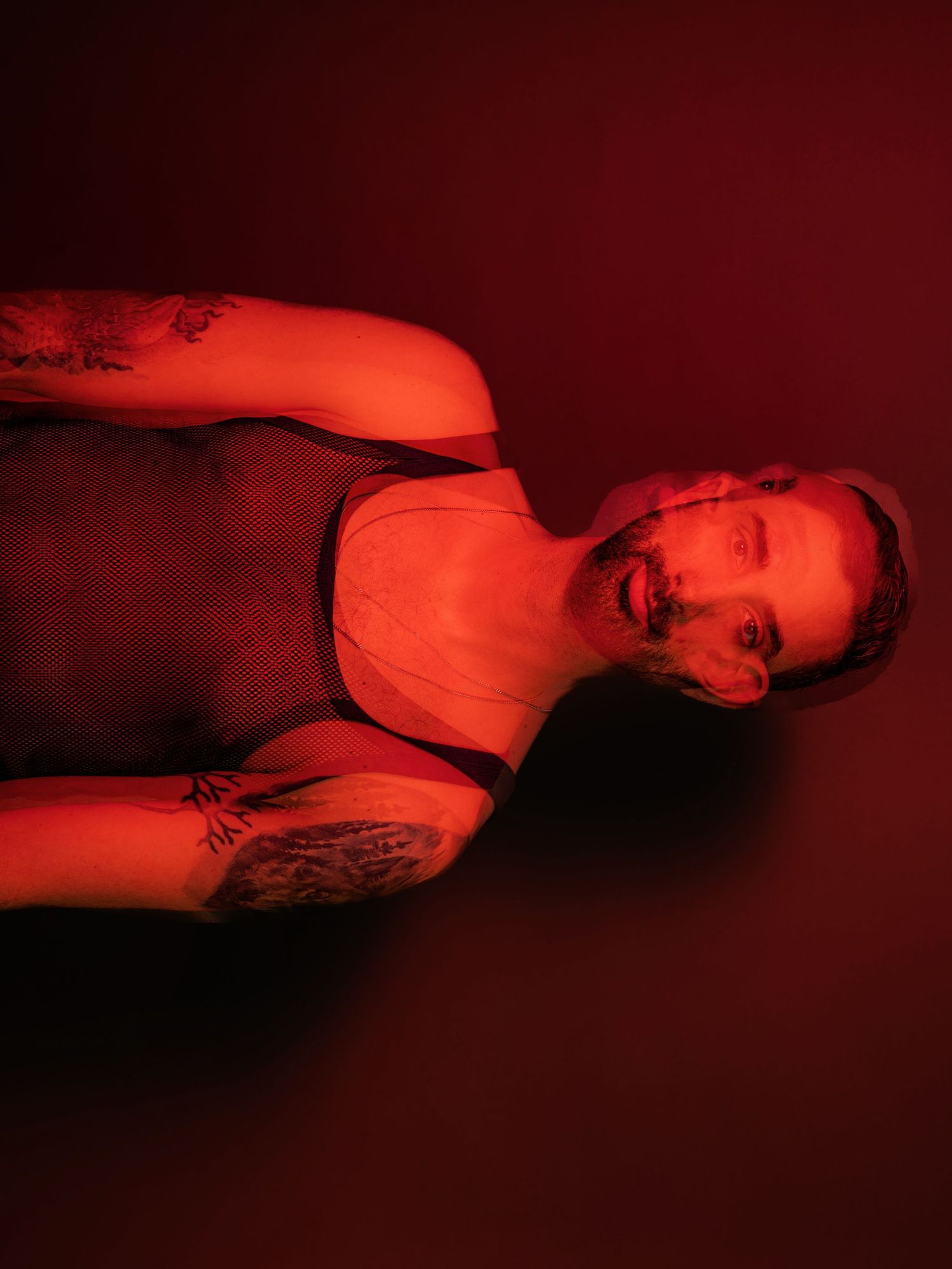 A person lying on their back with tattoos visible, illuminated by a reddish-orange light.