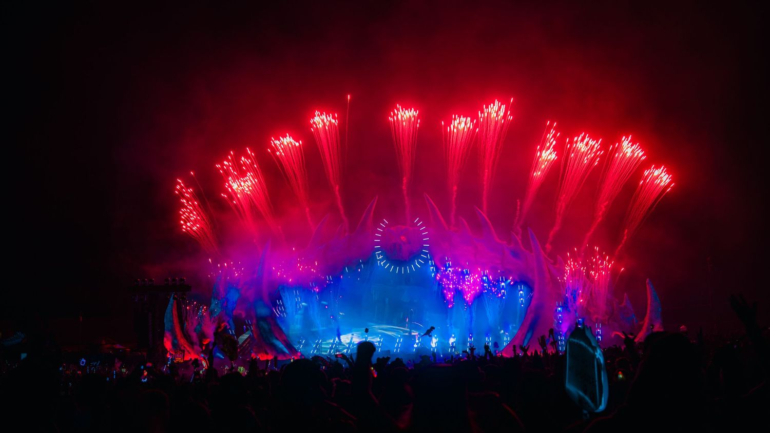 A panoramic view of a concert stage illuminated with vibrant red and blue lights creating a dramatic nighttime atmosphere.