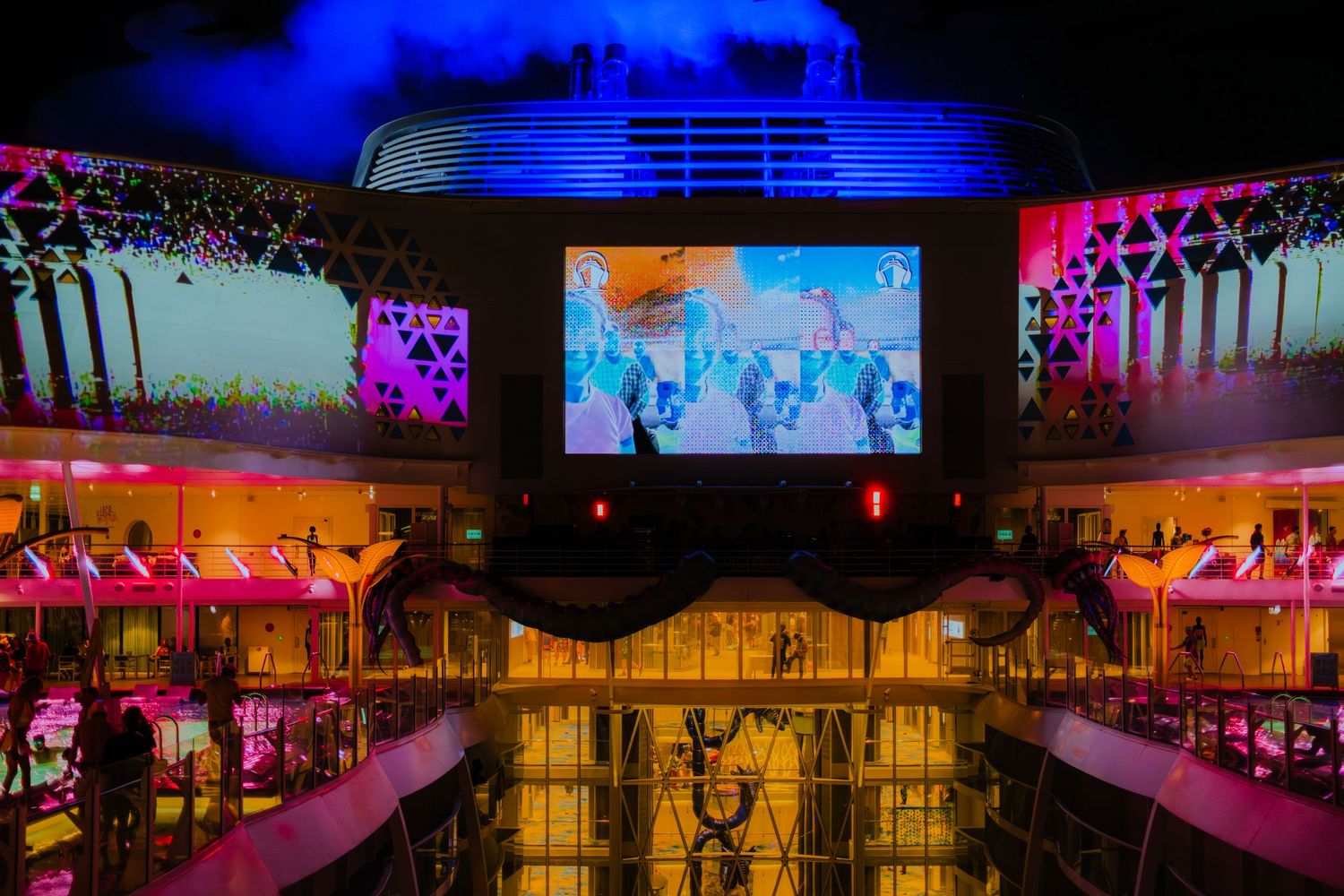 Colorful nightclub interior with large video screen display and neon lighting illuminating multiple levels of the venue.