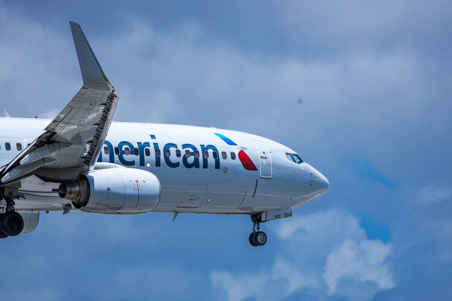American Airlines Boeing 737 aircraft on final approach against a partly cloudy blue sky.