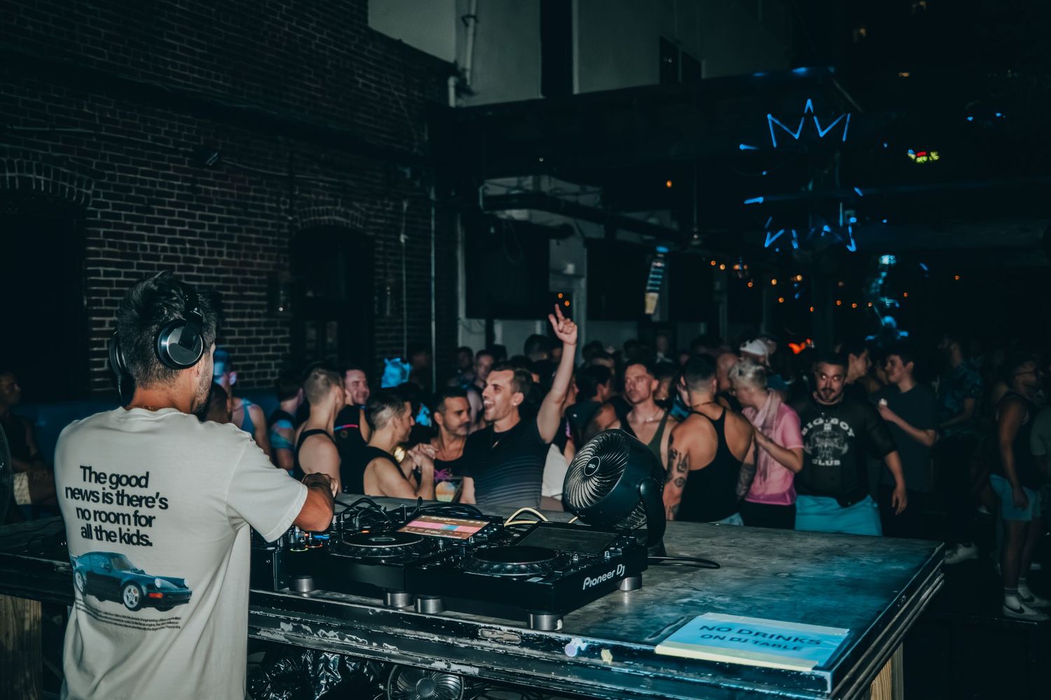 A DJ performs at a nightclub while a crowd of people dance and enjoy the music on a dark dance floor.