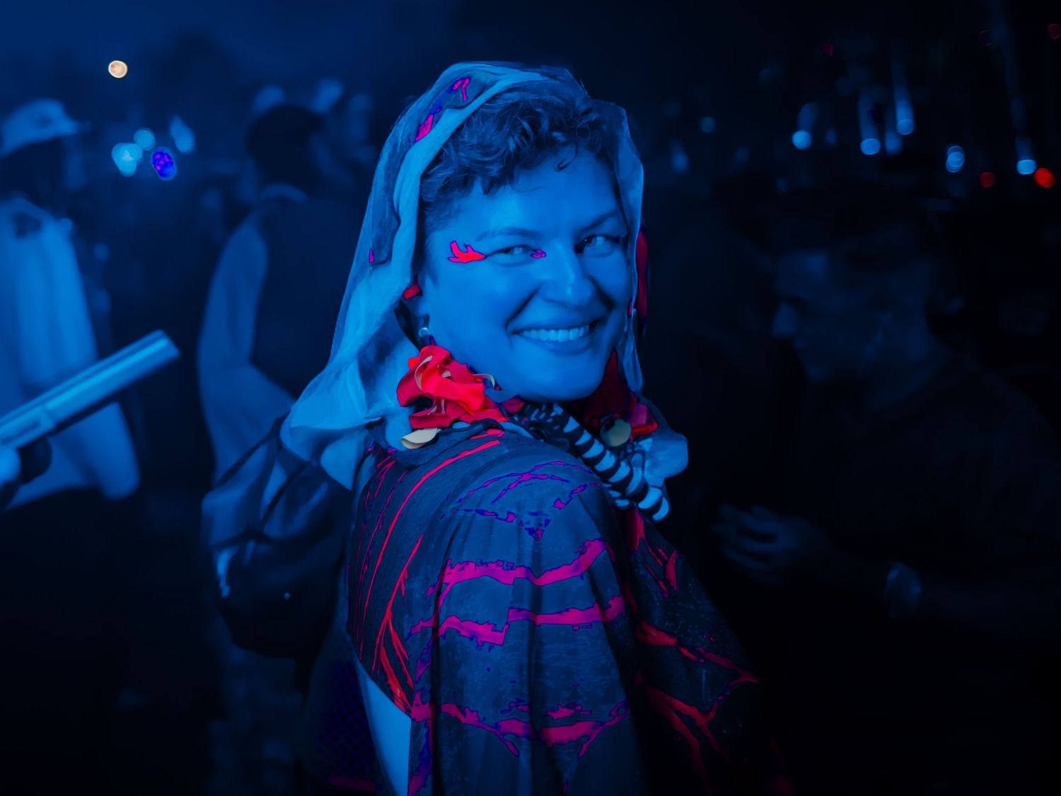 A performer in a dark blue-lit environment wearing a pink and purple outfit on stage during a show.