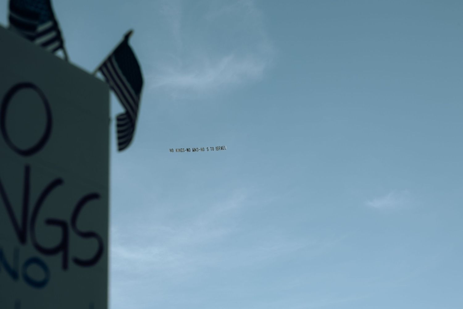 A small black speck appears in the cloudy blue sky above a partially visible green sign.