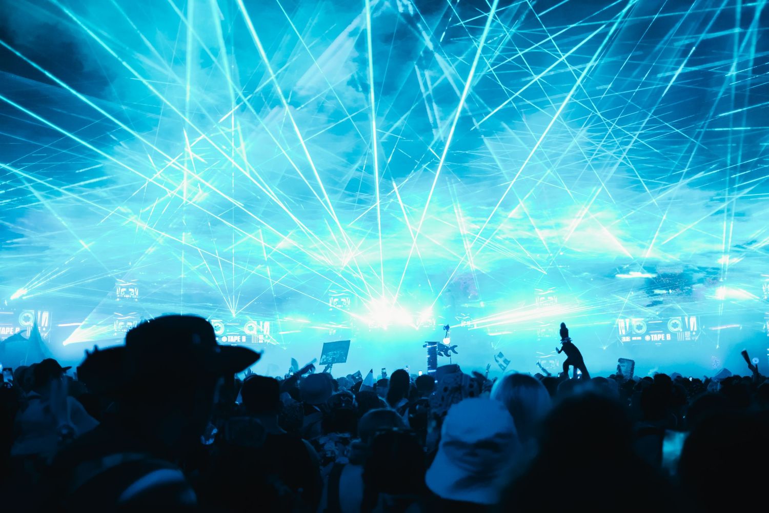 Concert crowd silhouettes against bright blue laser light show illuminating an energetic stadium performance.
