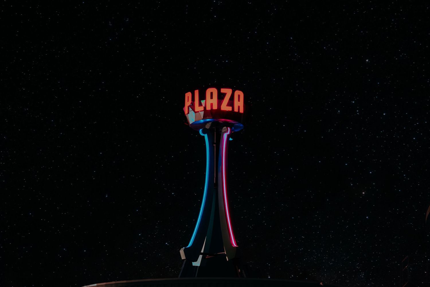 Neon Plaza sign glowing in red, blue, and pink against a dark starry night sky.