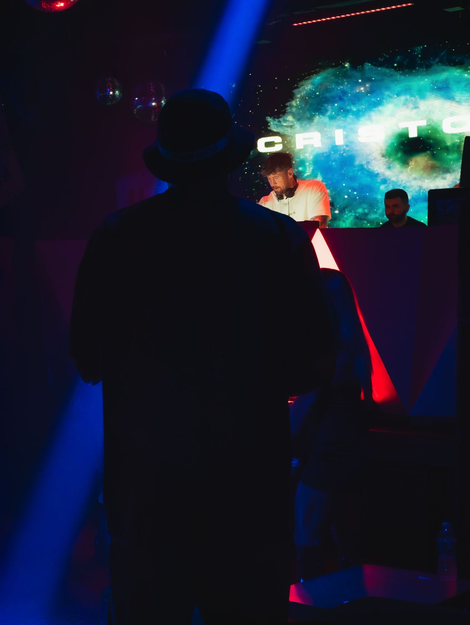 Silhouettes of people in a dark nightclub with blue lighting and a turquoise fog effect in the background.