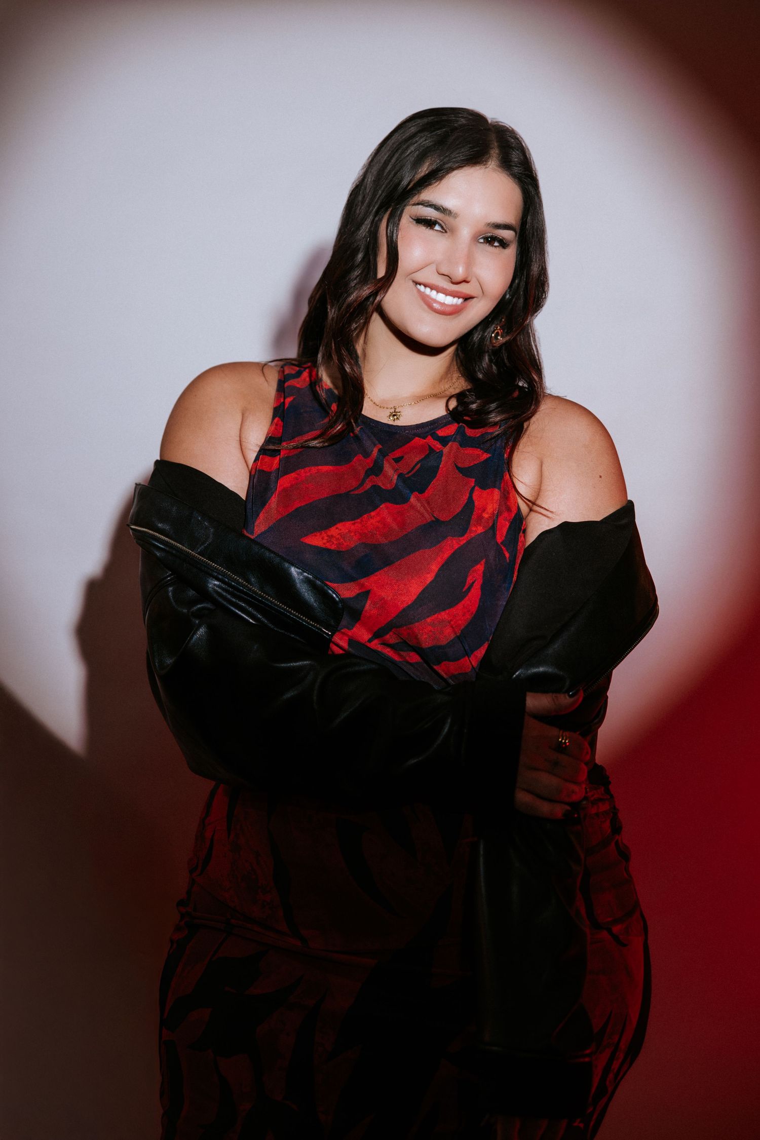Young woman smiling in red zebra-print dress with black gloves, posing against a red and white lit background.