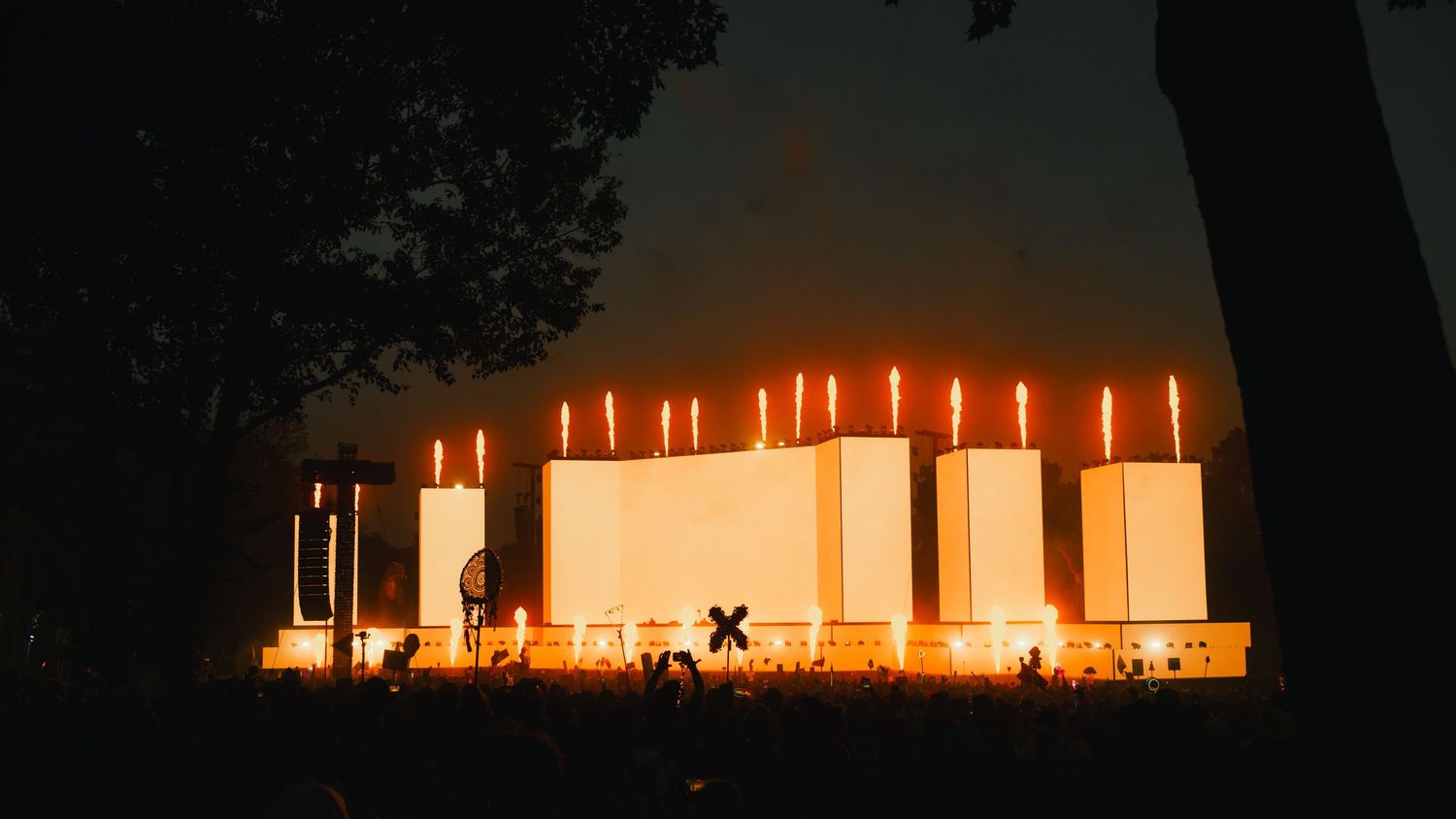Minimalist outdoor festival stage glows with warm orange vertical lights against a dark evening sky.