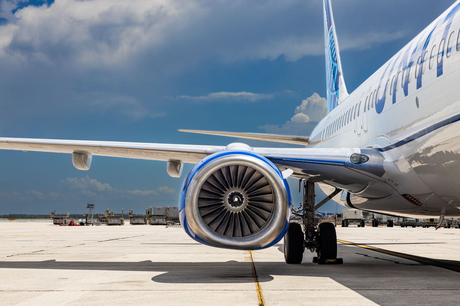 Close-up view of a commercial airplane jet engine and wing on a sunny airport tarmac with blue cloudy sky.